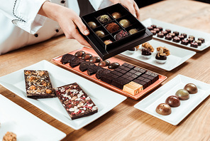 cropped view of chocolatier holding box with tasty and fresh made chocolate candies