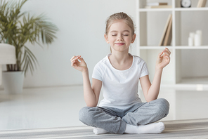 smiling little child meditating in lotus pose at home