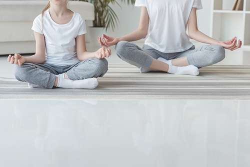 cropped shot of mother and daughter meditating in lotus pose together at home