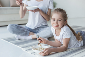 mother and daughter eating cereal meal while relaxing on yoga mats after exercising