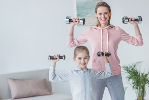 fit mother and daughter working out with dumbbells at home