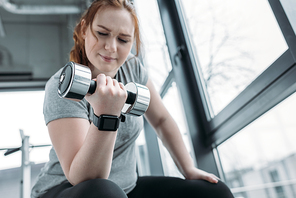 Curvy girl training biceps with dumbbell in gym