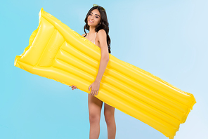 slim young woman posing with yellow inflatable mattress, isolated on blue