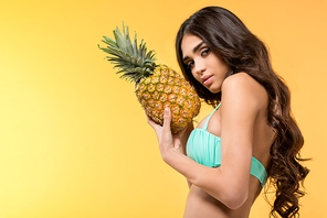 beautiful woman in bikini holding fresh pineapple, isolated on yellow