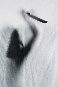 scary blurry silhouette of person holding knife behind veil