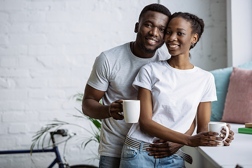 유토이미지 | happy young african american couple holding cups and smiling at ...