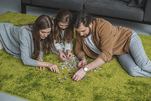 high angle view of parents and daughter connecting puzzle pieces on carpet in living room