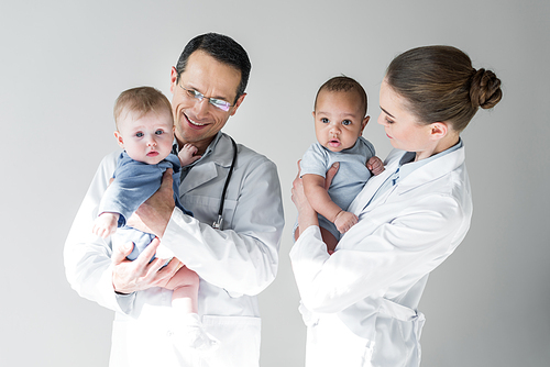 happy pediatricians holding little babies isolated on grey