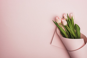 top view of tulips wrapped in paper on pink background
