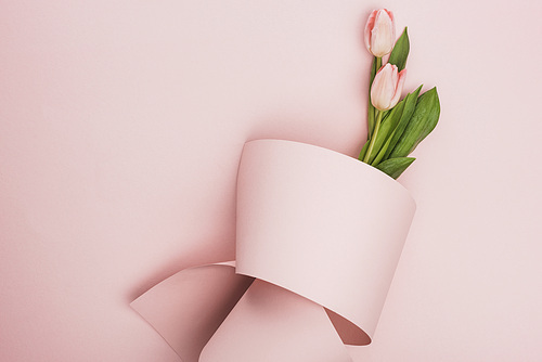 top view of tulip bouquet wrapped in paper swirl on pink background