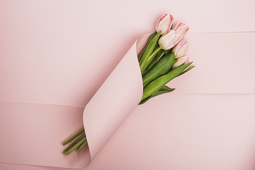 top view of tulip bouquet wrapped in paper swirl on pink background