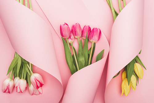 top view of pink and yellow tulips wrapped in paper spiral swirls on pink background
