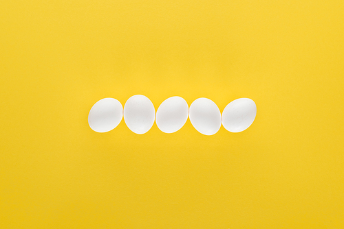 five white chicken eggs in row on yellow background