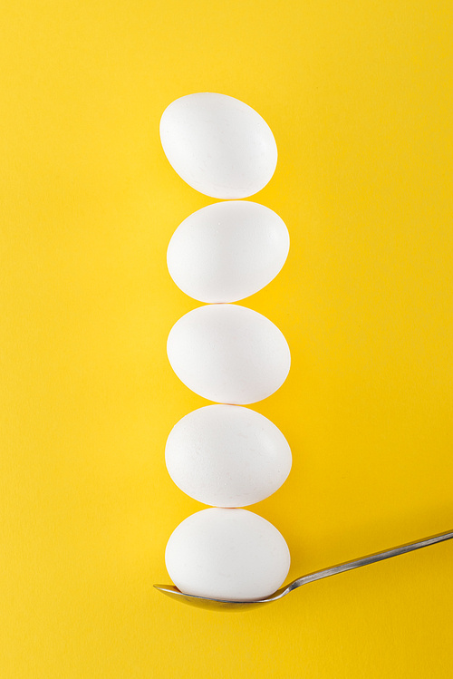 five white chicken eggs on spoon on yellow background