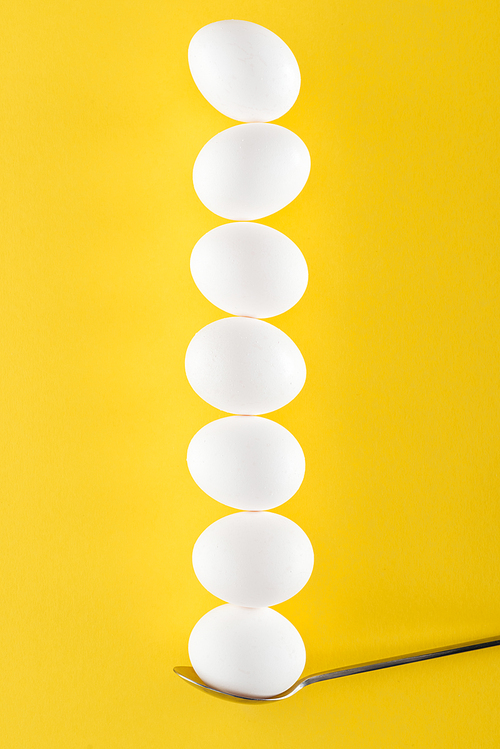 seven white chicken eggs on spoon on yellow background