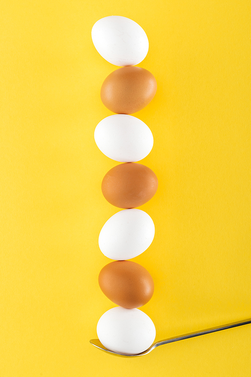 seven white and brown chicken eggs on spoon on yellow background