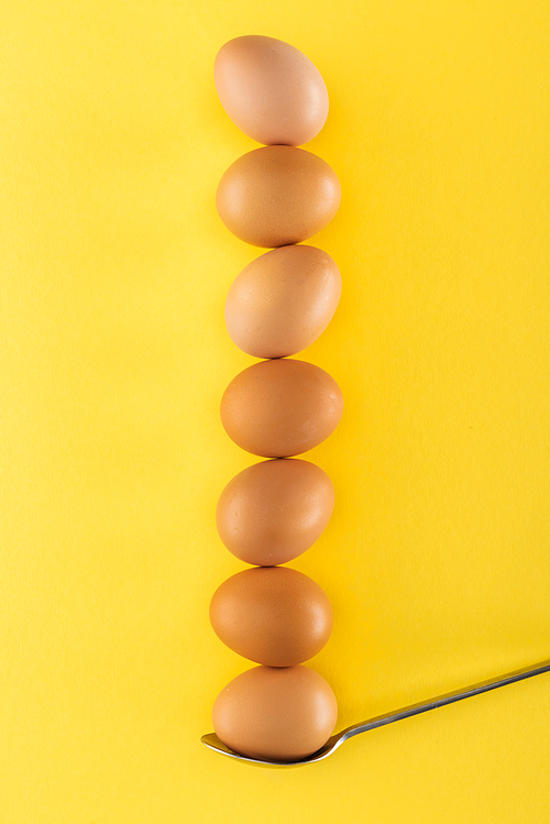 seven brown chicken eggs on spoon on yellow background