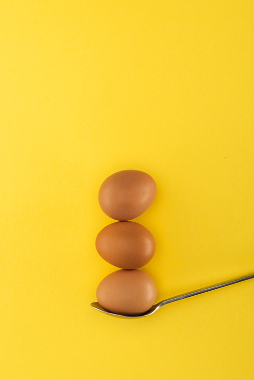 three brown chicken eggs on spoon on yellow background