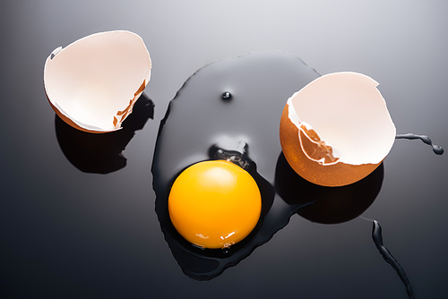 close up of fresh smashed egg with yolk, protein and eggshell on black background