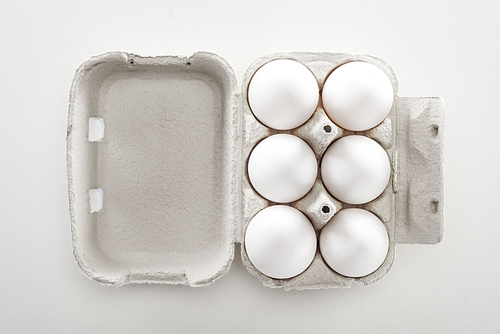 top view of raw white chicken eggs in carton box on white background