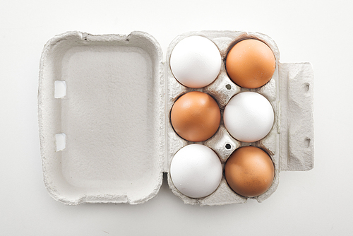 top view of raw white and brown chicken eggs in carton box on white background
