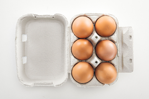 top view of raw brown chicken eggs in carton box on white background