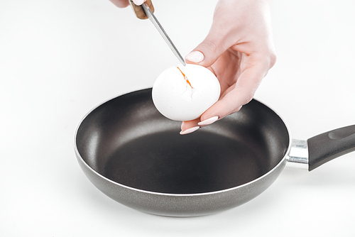 cropped view of woman smashing egg into pan with knife on white background