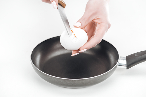 partial view of woman smashing egg into pan with knife on white background