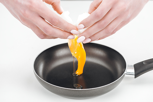 cropped view of woman smashing chicken egg into pan on white background