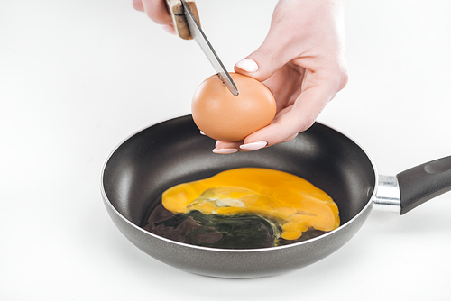 cropped view of woman smashing chicken egg with knife while preparing scrambled eggs in pan on white background