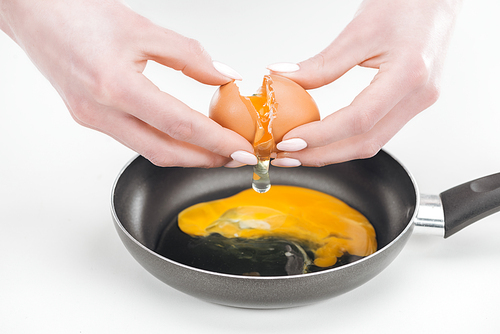 partial view of woman smashing chicken egg while preparing scrambled eggs in pan on white background