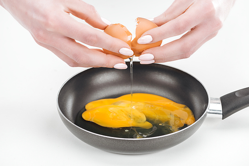 cropped view of woman smashing fresh chicken egg while preparing scrambled eggs in pan on white background