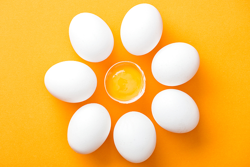 top view of whole white eggs and smashed one with yolk on bright orange background
