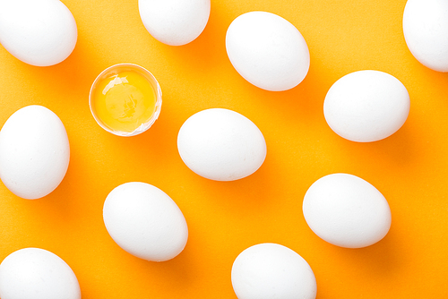 top view of whole white fresh chicken eggs with smashed one on bright orange background