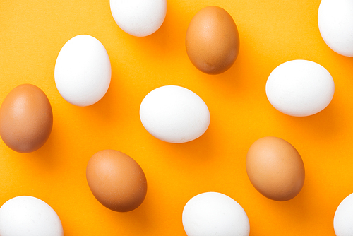 top view of whole white and brown fresh chicken eggs on bright orange background