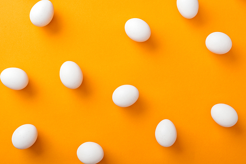 top view of whole white fresh chicken eggs on bright orange background