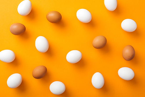 top view of whole white and brown organic chicken eggs on bright orange background