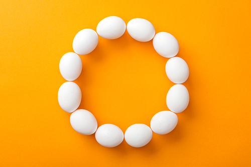 top view of whole white organic chicken eggs arranged in round frame on bright orange background with copy space