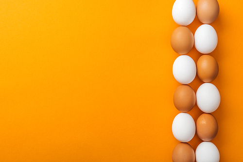 top view of white and brown organic chicken eggs on bright orange background with copy space