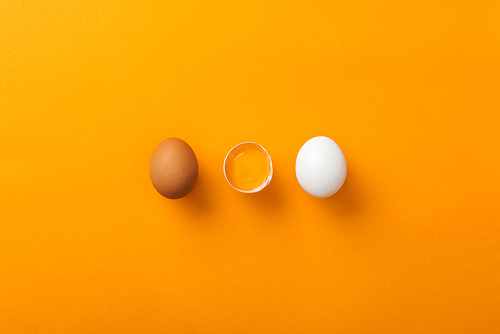 top view of two whole chicken eggs with smashed one on bright orange background
