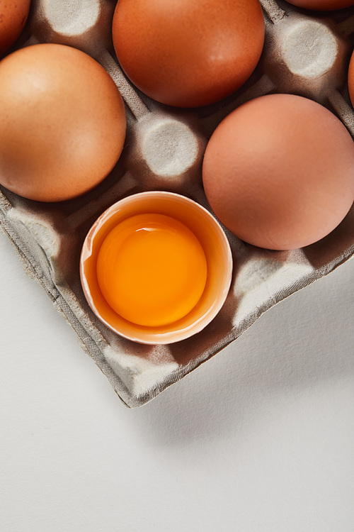 top view of broken eggshell with yellow yolk near eggs in carton box