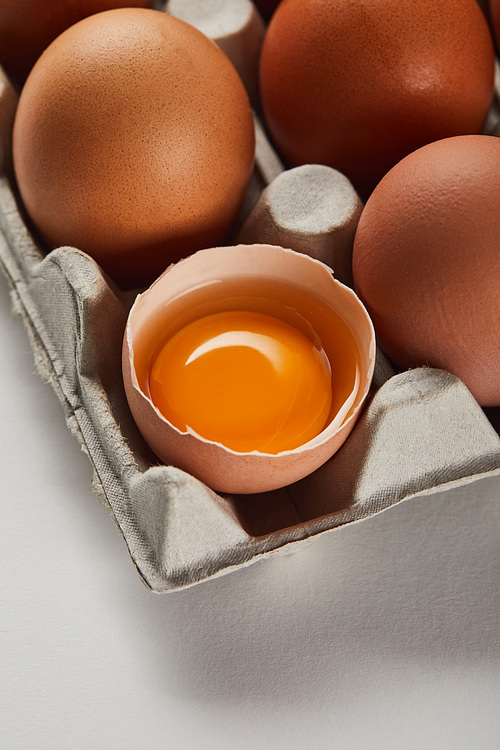 broken eggshell with yellow yolk near eggs in carton box