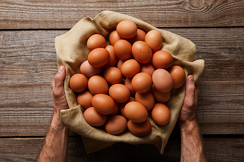 top view of man holding chicken eggs in cloth over wooden table