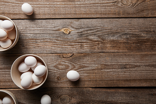 top view of chicken eggs in bowls on wooden table