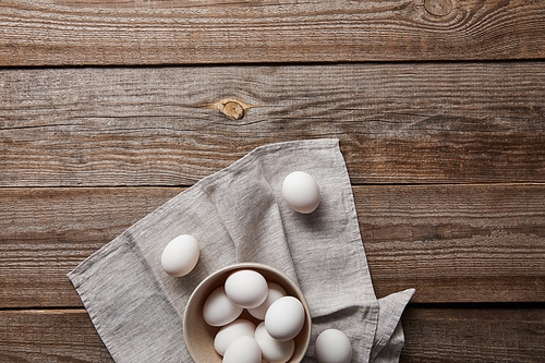 top view of chicken eggs in bowl on wooden table with cloth