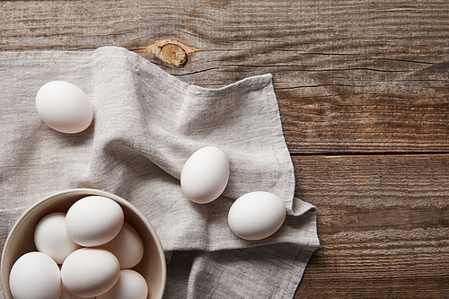 top view of chicken eggs in bowl on wooden table with cloth