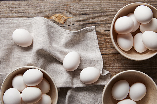 top view of chicken eggs in bowls on wooden table with cloth