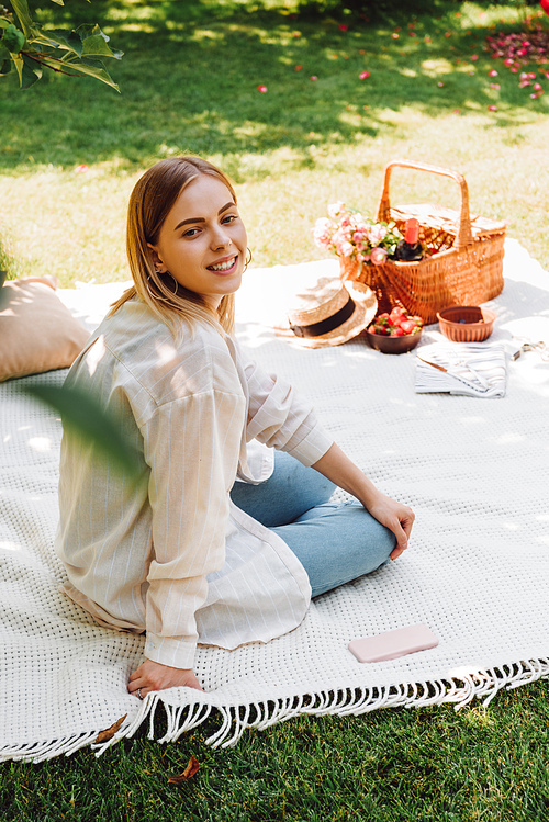 happy blonde girl sitting on blanket in garden and having picnic at sunny day