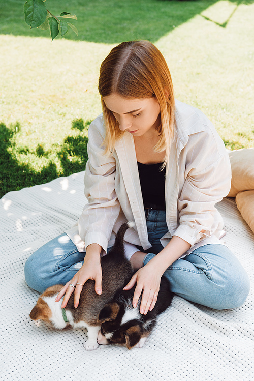 blonde girl sitting on blanket in garden with cute puppies at sunny day