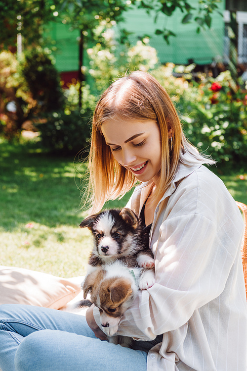 happy blonde girl sitting on blanket in garden with adorable puppies at sunny day